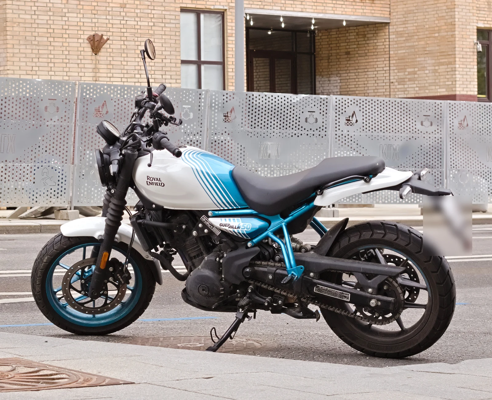 White and turquoise Royal Enfield Guerrilla 450 parked on its side stand beside a brick building in Moscow