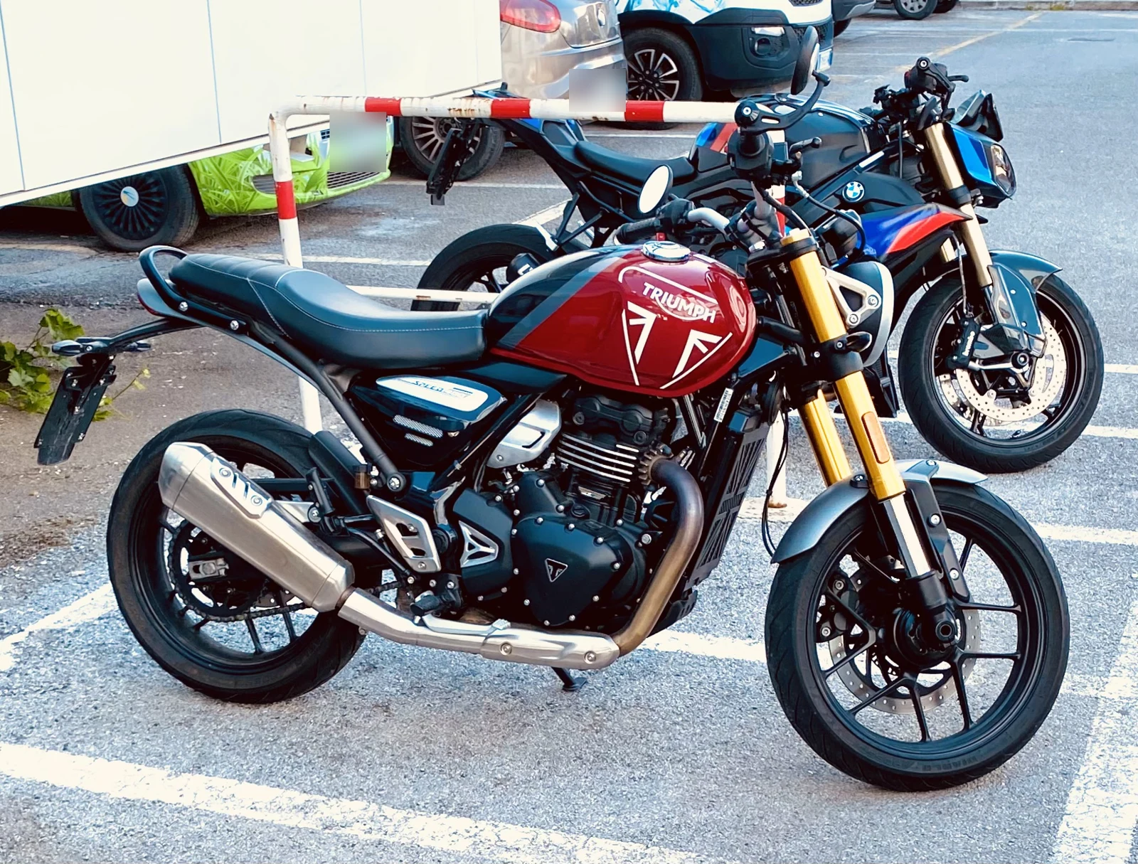 Red Triumph Speed 400 with gold front forks parked beside a blue motorcycle in an outdoor car park