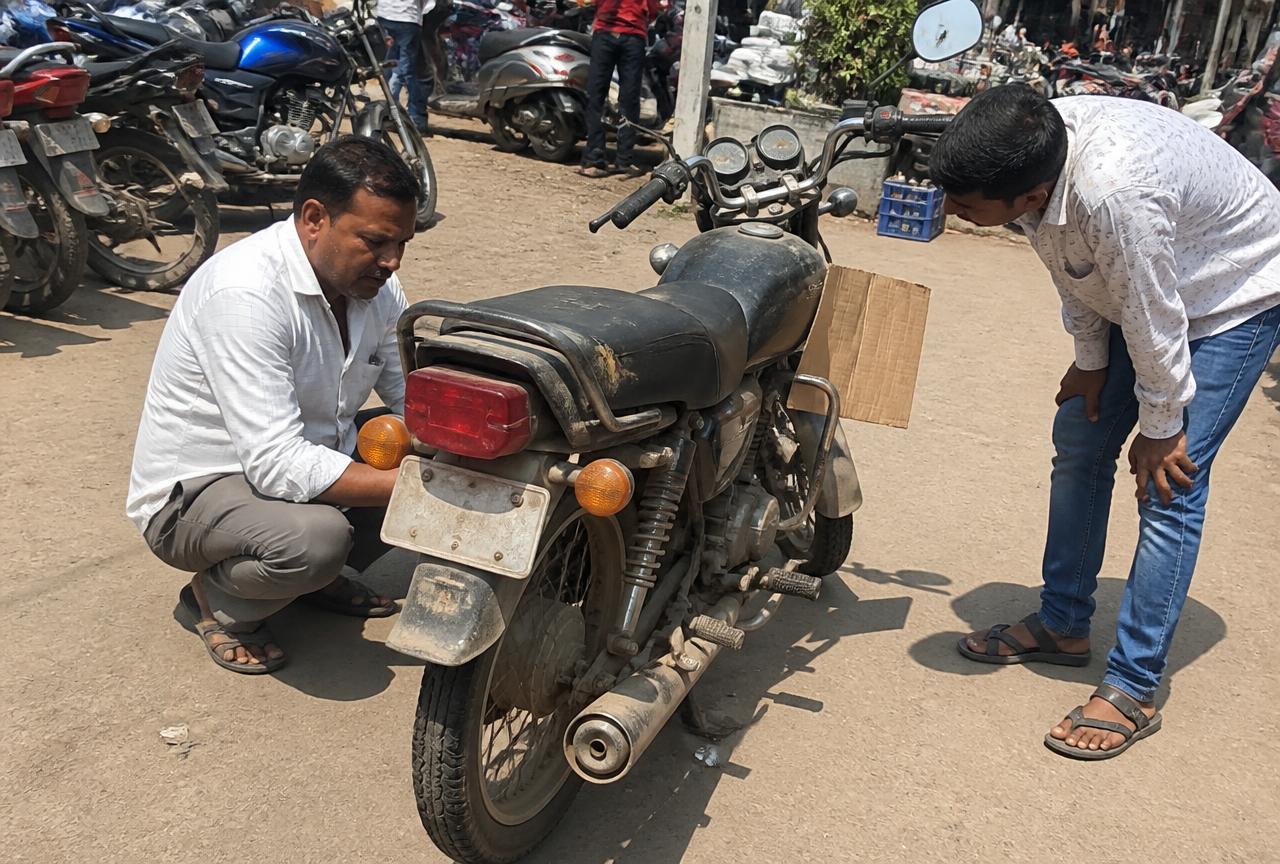 Buyer and seller inspecting a dusty used motorcycle at a roadside second-hand bike market in India